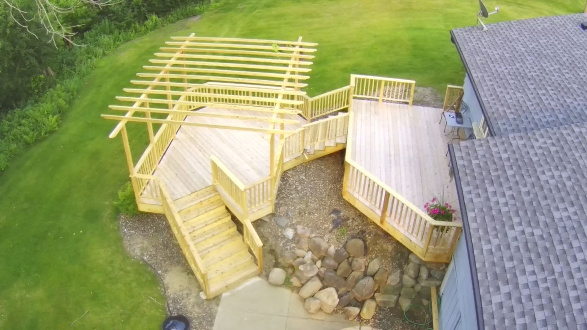Wooden deck with stairs, built-in seating, and pergola extending from a house, set in a grassy yard.