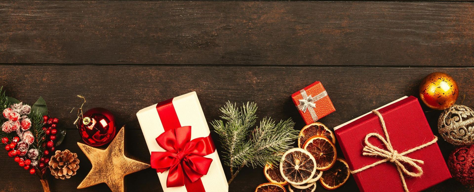 A festive holiday scene featuring wrapped gifts, pine branches, and ornaments on a dark wooden backg