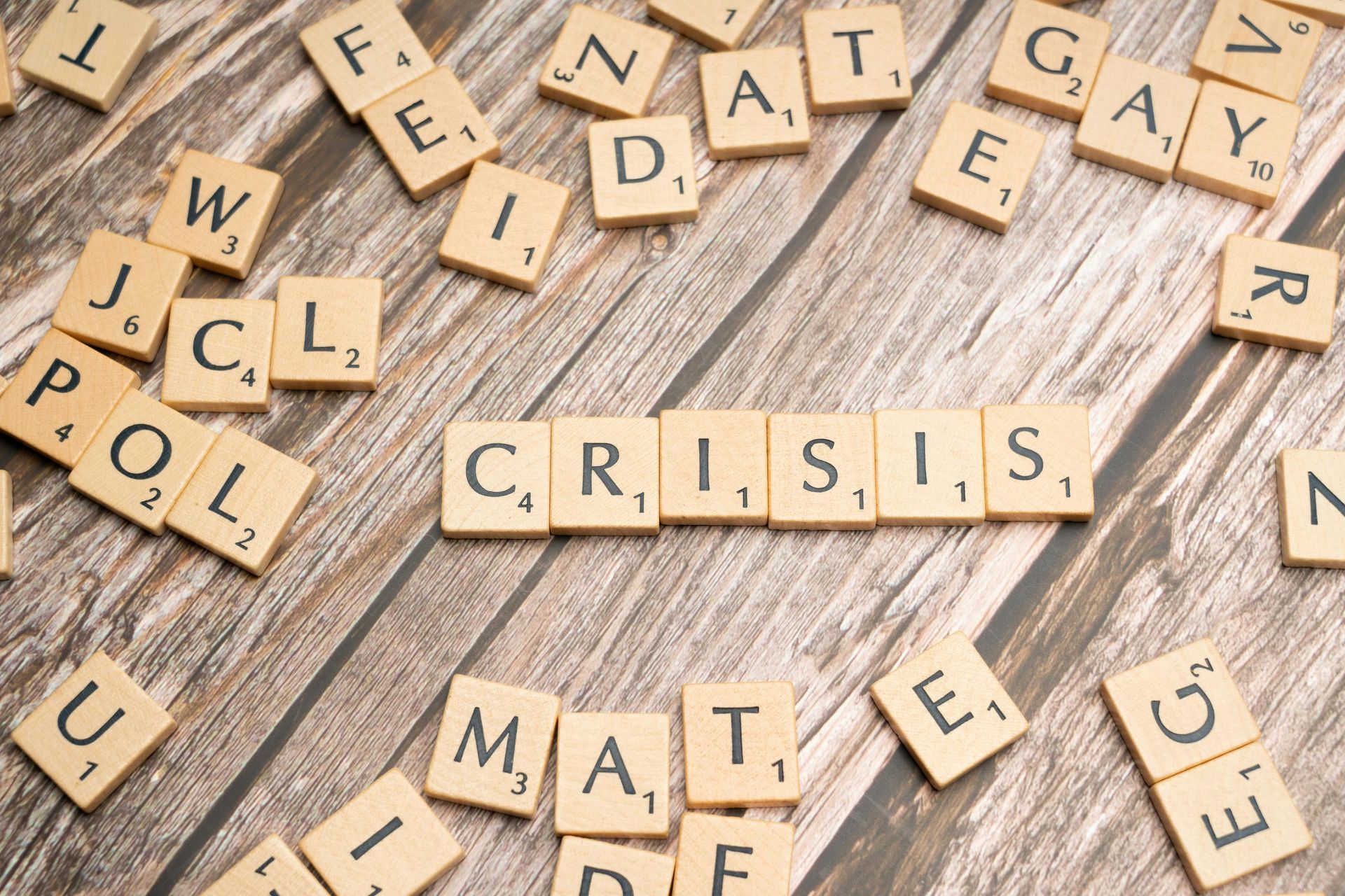 Scrabble tiles scattered on a wooden surface, with the word 'CRISIS' spelled out in the center.