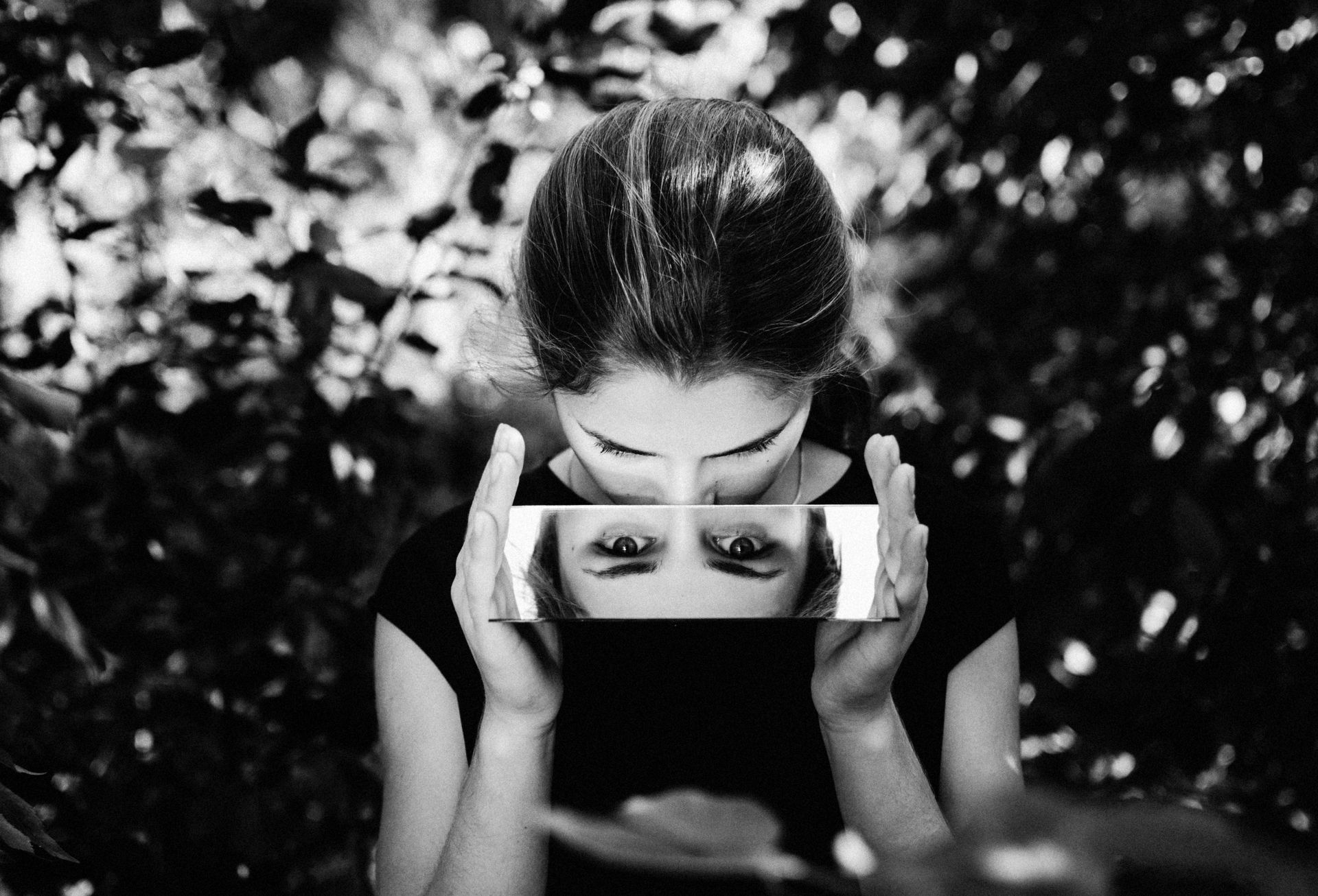 Black and white photo of a woman holding a mirror in front of her face, reflecting her upside-down i