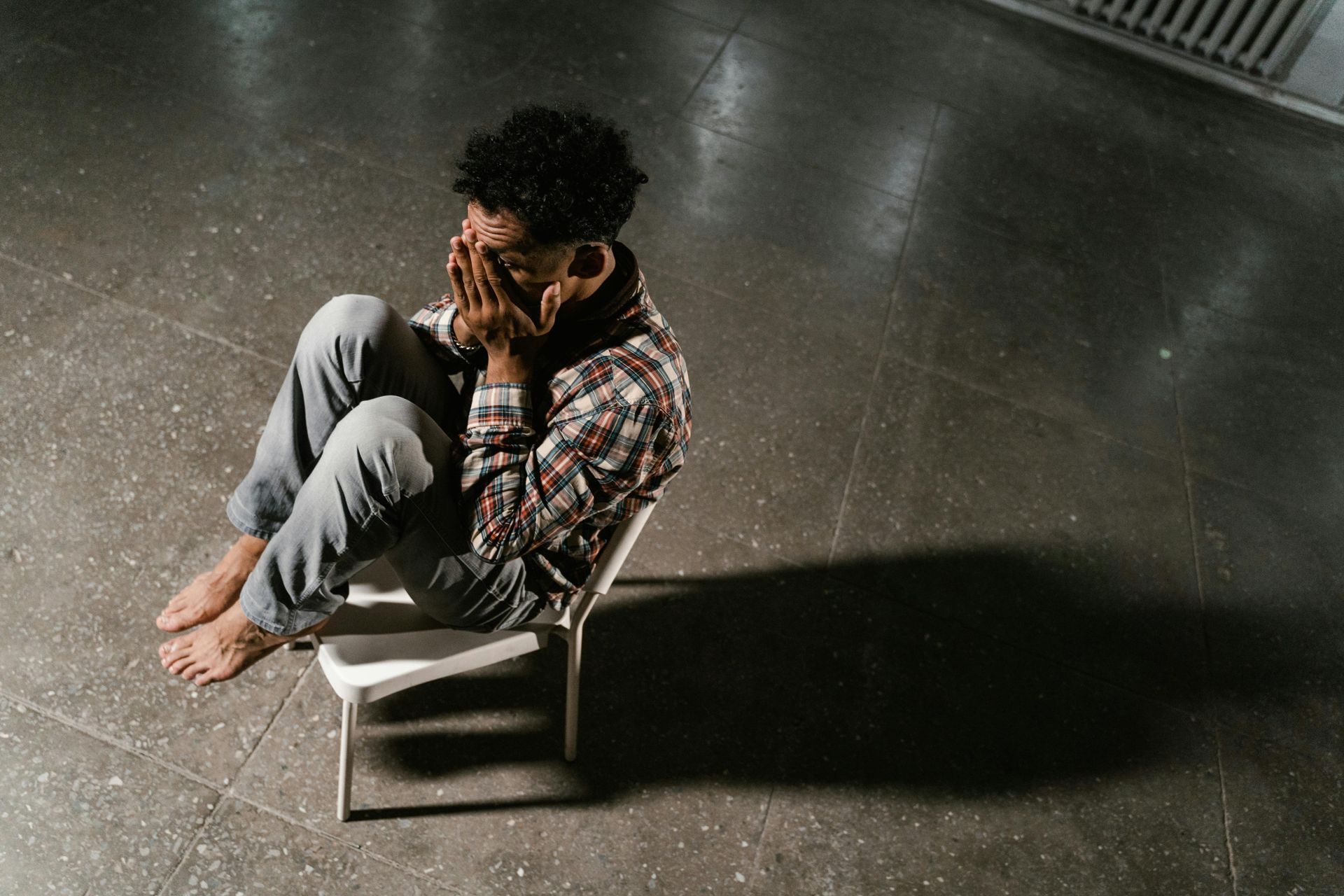 Person on a chair in a dim room, appearing overwhelmed, symbolising the emotional weight of anxiety