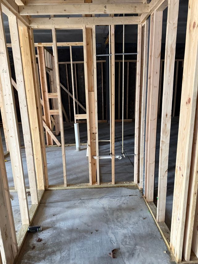 Interior of a house under construction with exposed wooden framing and unfinished concrete floor