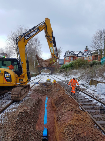 Yellow excavator and worker in orange gear repairing railway tracks in a snowy construction area.