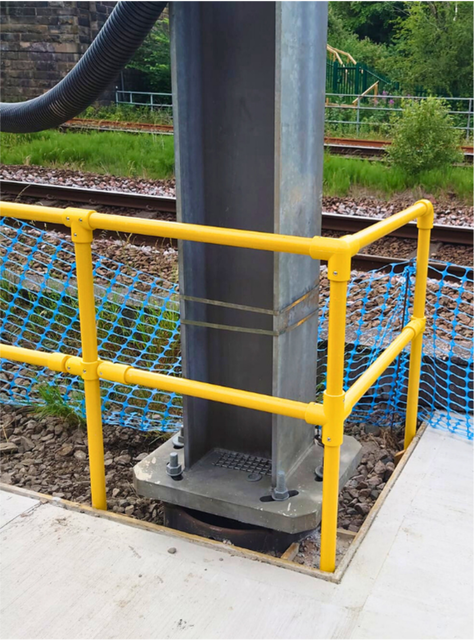 Yellow safety railing around a steel pole base beside a train track and walkway