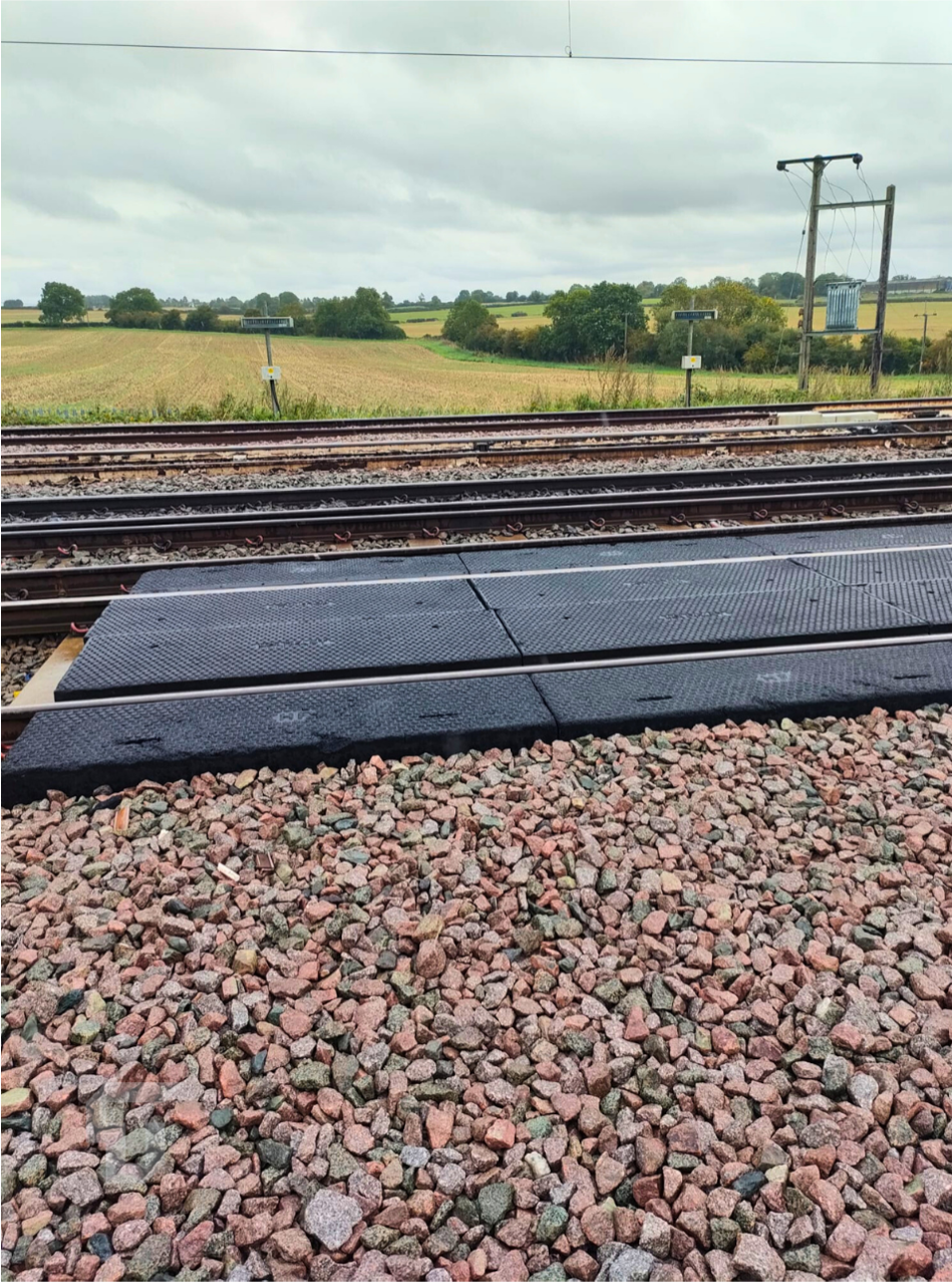Railroad tracks beside a rural field, with gravel foreground and overcast sky.
