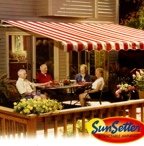People sit at a table under a red and white striped awning on a deck, enjoying a meal.  SunSetter logo in the foreground.