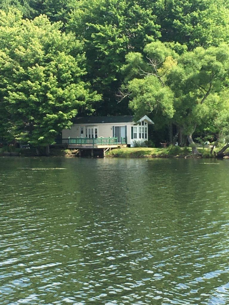 A small house sits on a small island in the middle of a lake surrounded by trees.