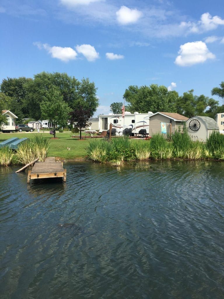 A dock in the middle of a lake with a rv parked in the background