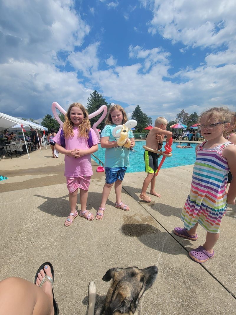 A group of children and a dog are standing next to a pool