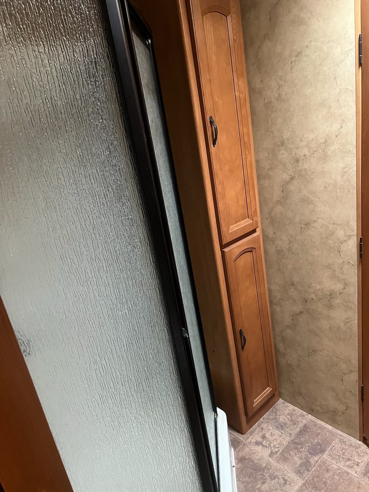 A bathroom with wooden cabinets and a glass door