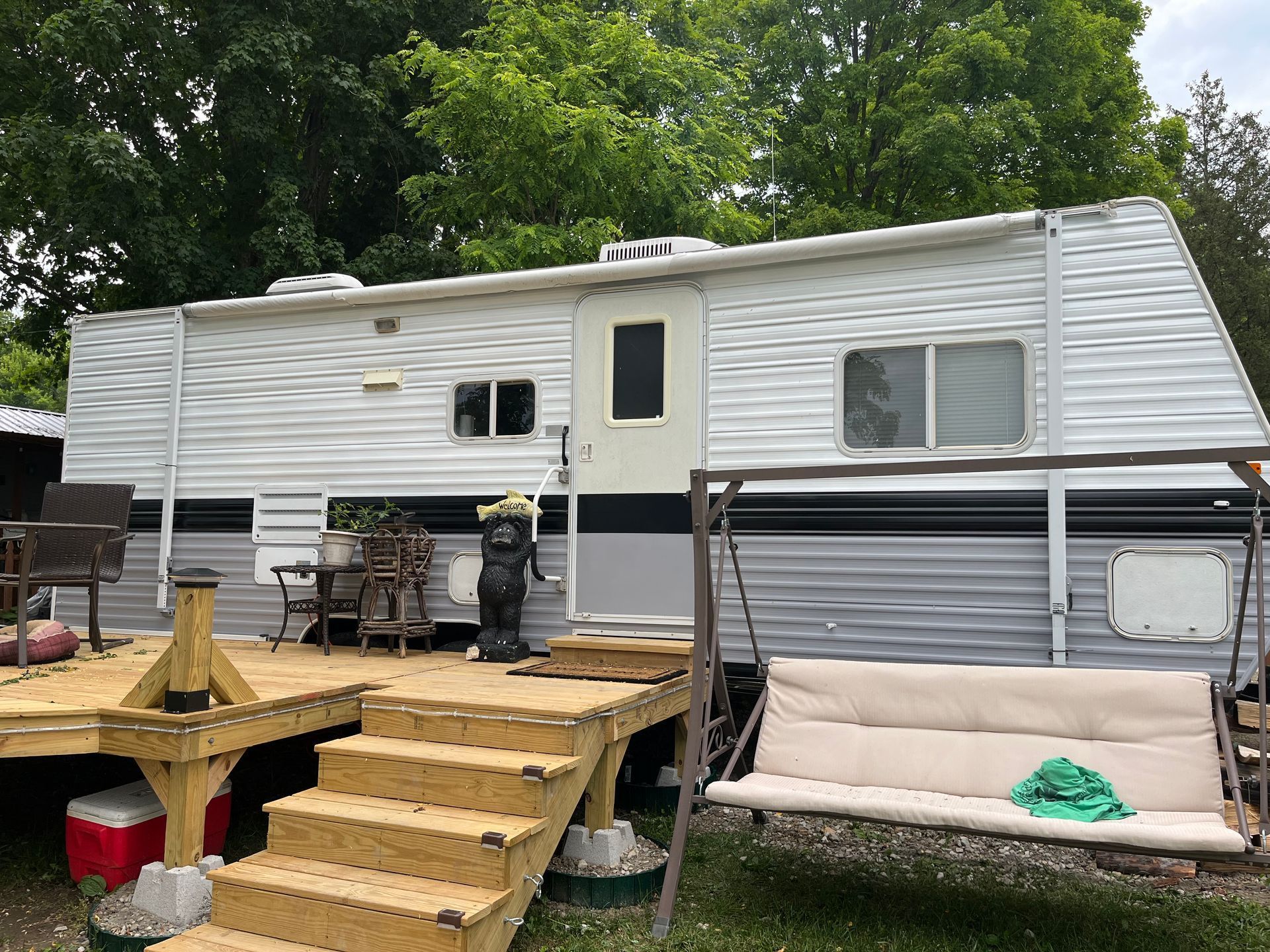 A white trailer with a wooden deck and swing in front of it