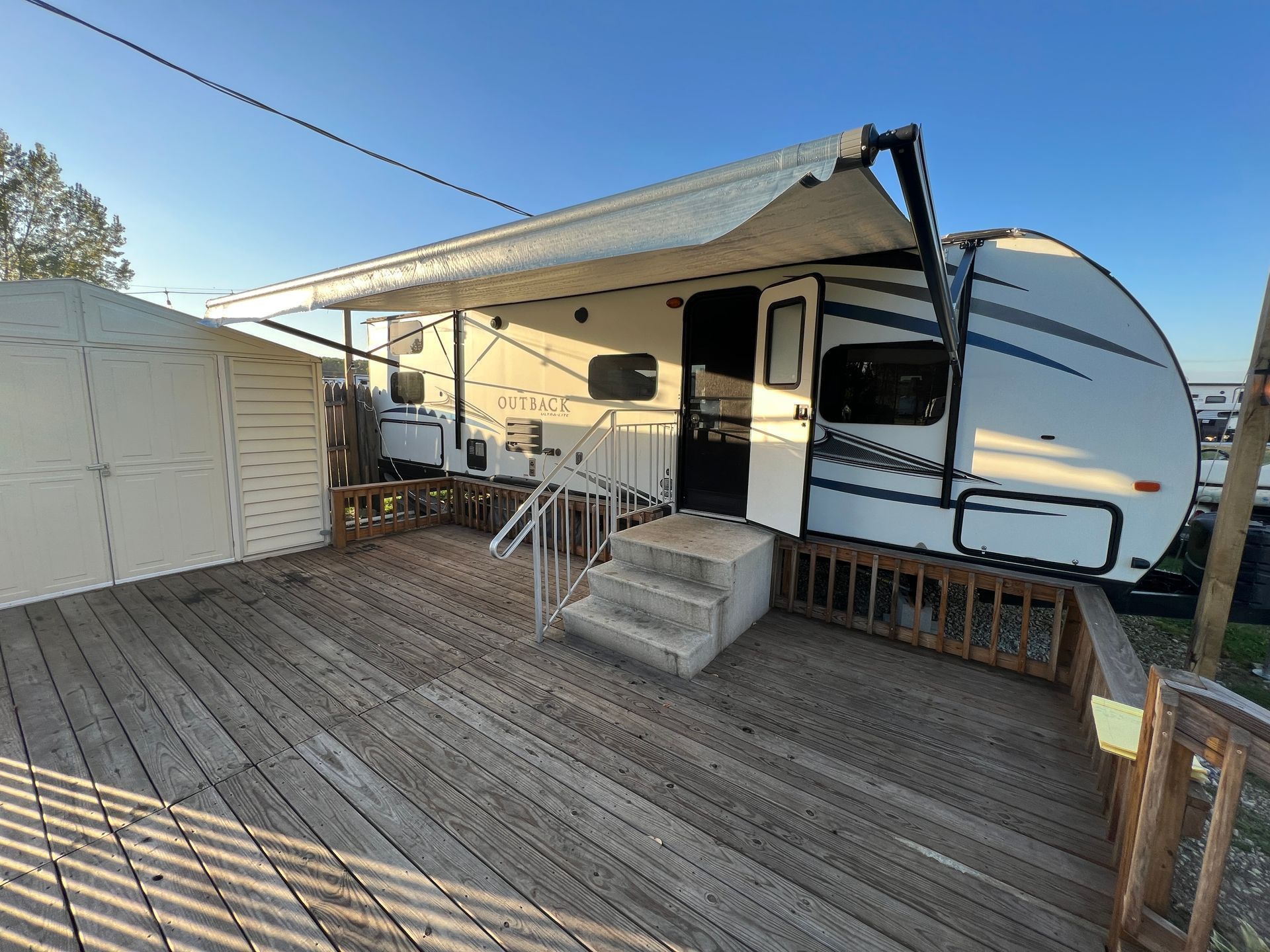 A white trailer with a canopy is parked on a wooden deck