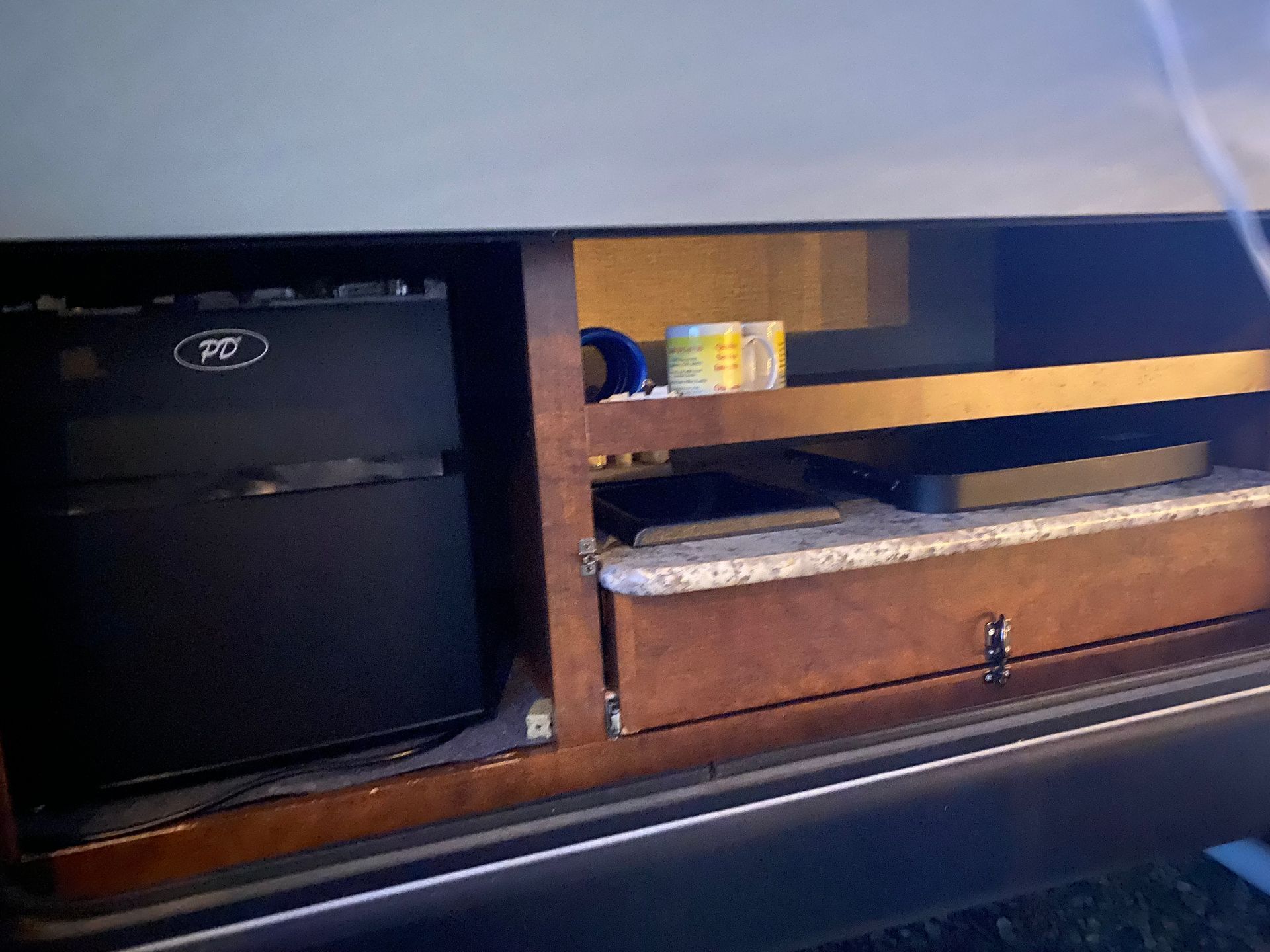 A black fridge is sitting under a wooden shelf with a drawer underneath it