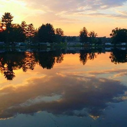 A sunset over a lake with trees reflected in the water