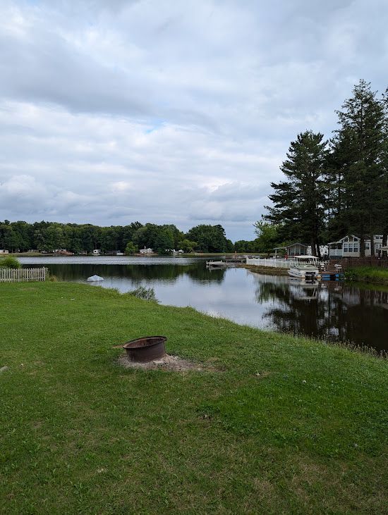 A lake surrounded by trees and grass with a fire pit in the foreground