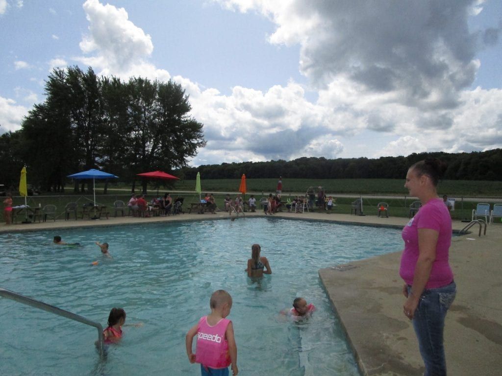 A woman in a pink shirt stands next to a swimming pool