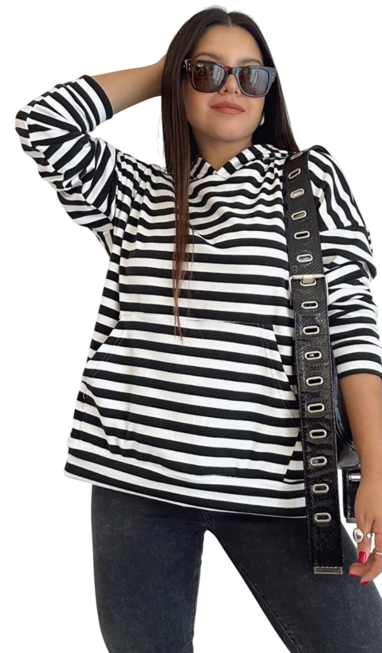 Mujer con sudadera con capucha a rayas y gafas de sol, llevando un bolso negro, posando al aire libre.