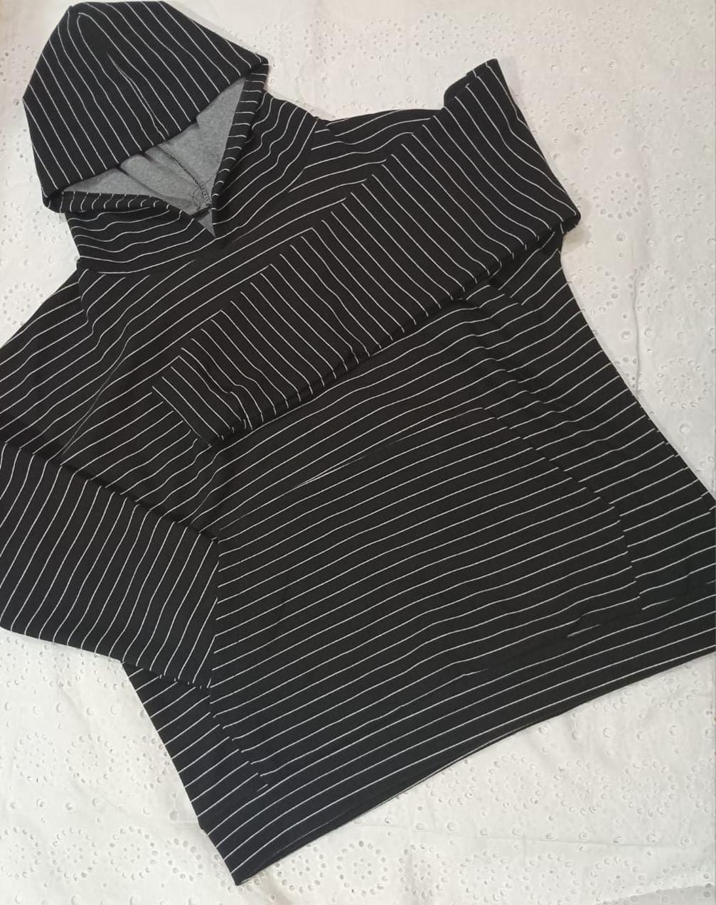 Mujer con sudadera con capucha a rayas y gafas de sol, llevando un bolso negro, posando al aire libre.