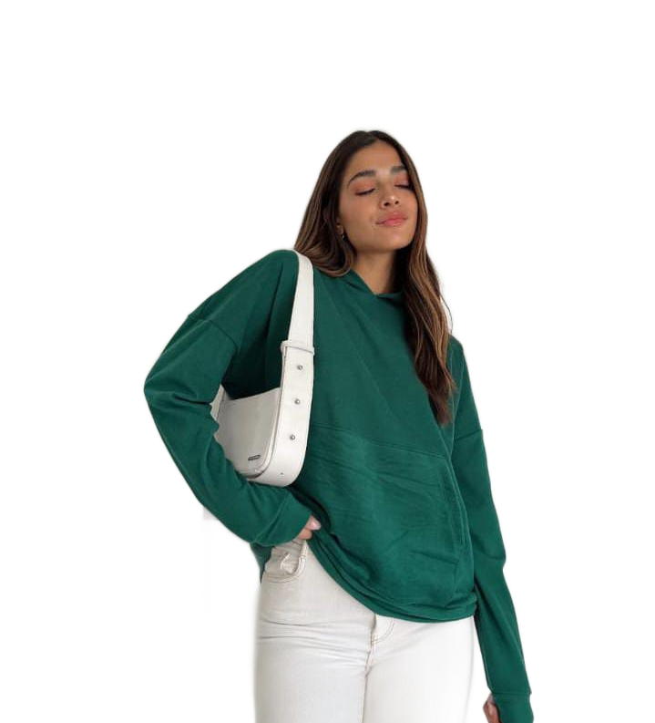 Mujer con sudadera con capucha verde y jeans blancos, llevando un bolso blanco, sonriendo.