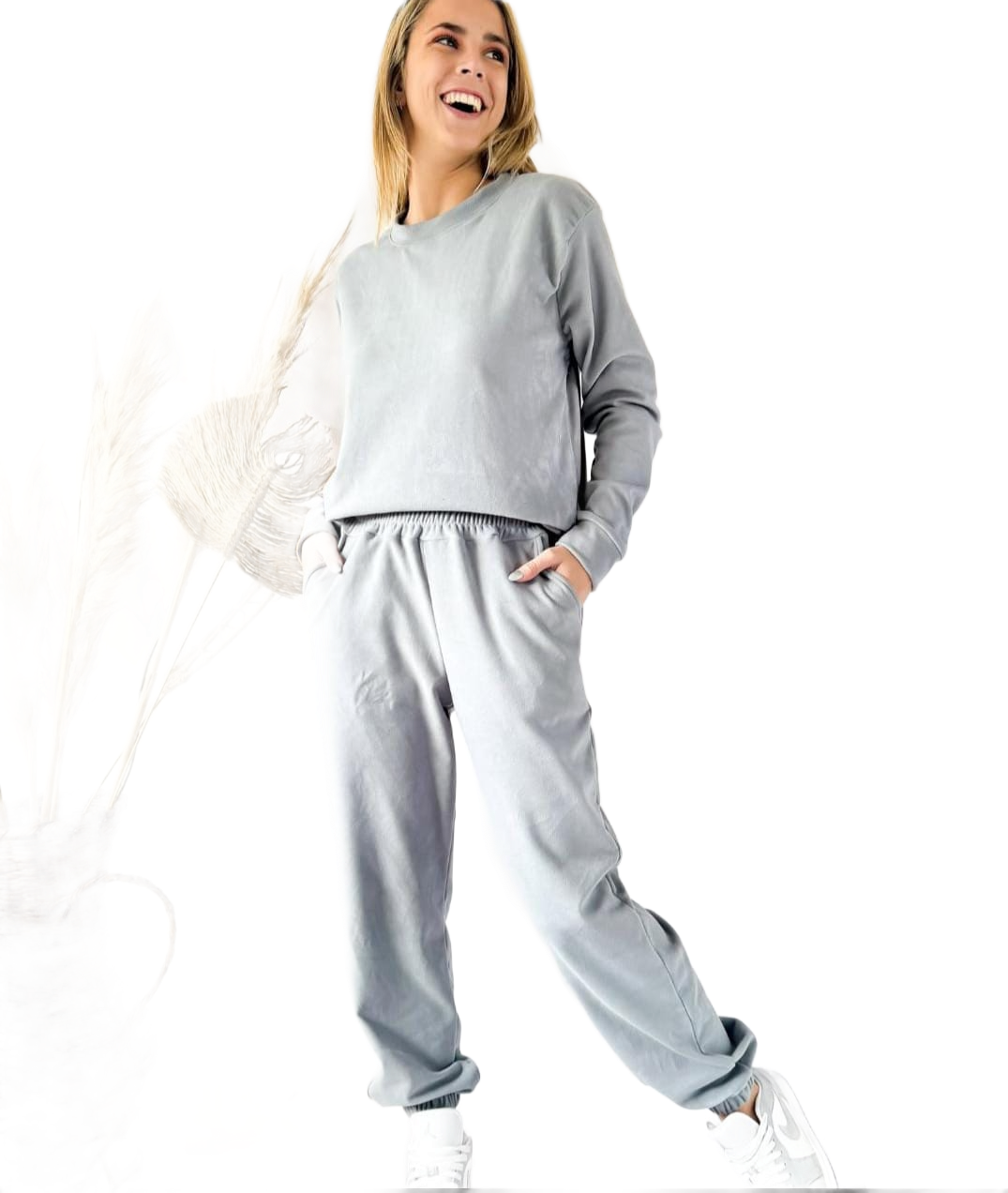 Mujer con sudadera verde y gorra de béisbol sonríe, con la mano en la gorra.