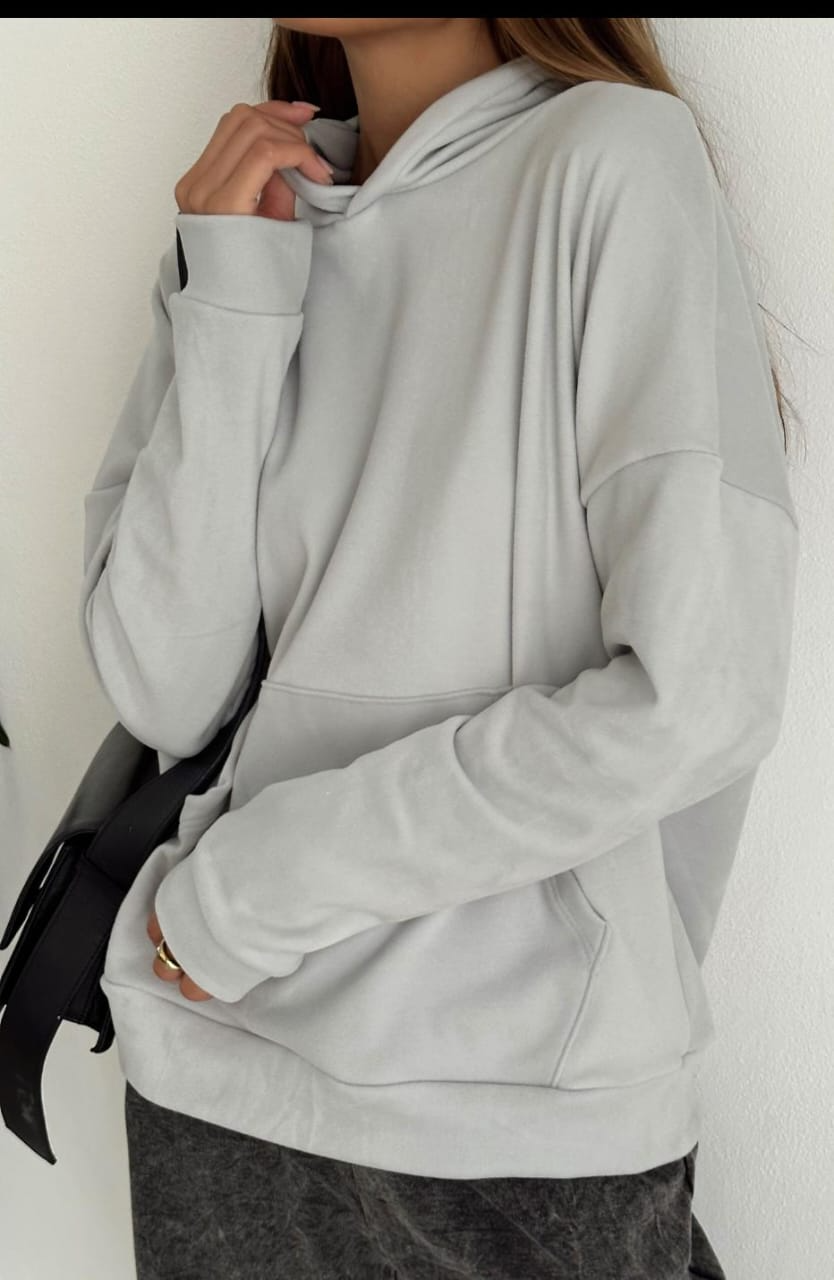 Mujer con sudadera con capucha verde y jeans blancos, llevando un bolso blanco, sonriendo.