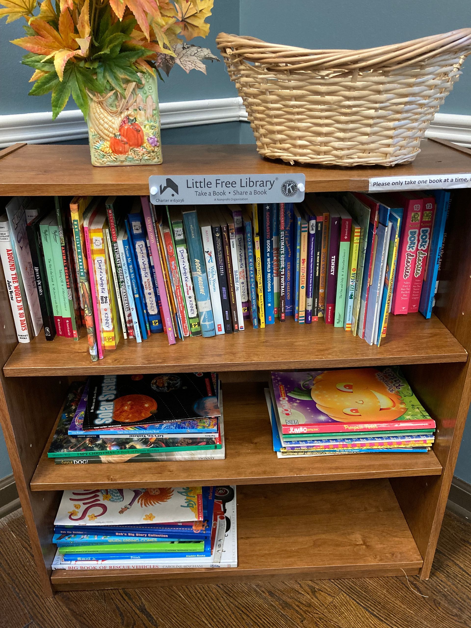 Bookshelf at the Little Free Library, showing Kiwanis BBP plaquard.