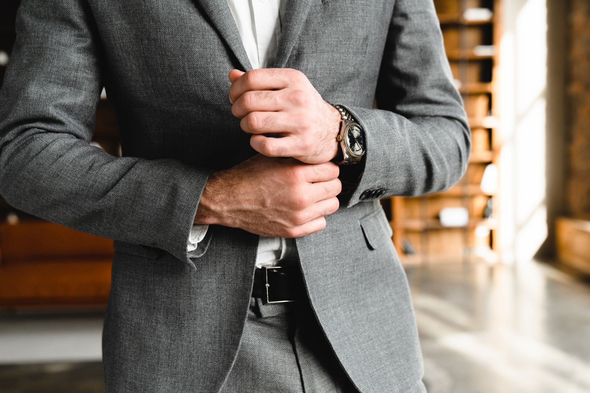 Close-up of a man in a gray suit adjusting his jacket indoors.