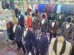 Mannequins in suits and jackets displayed in a clothing store with colorful shirts in the background