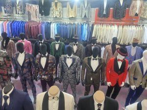 Clothing store display with rows of mannequins wearing colorful suits and jackets beneath hanging garments
