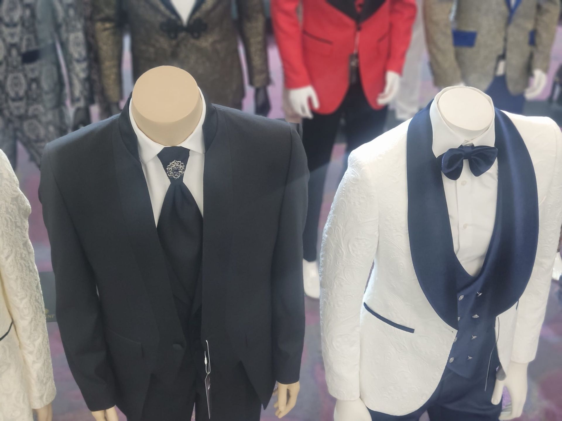 Two mannequins in formal suits: black tuxedo and white tuxedo with navy shawl lapels and bow tie.