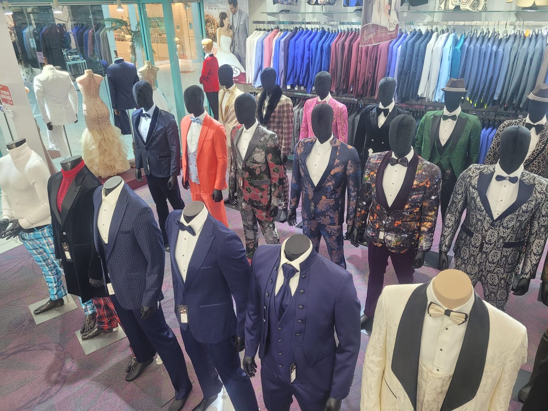 Mannequins displaying suits and jackets in a clothing store, with rows of colorful garments behind them