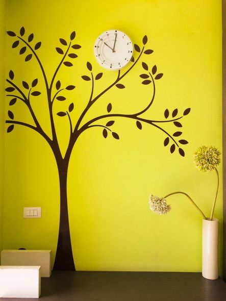 yellow wall with a tree wall sticker and a hanging clock