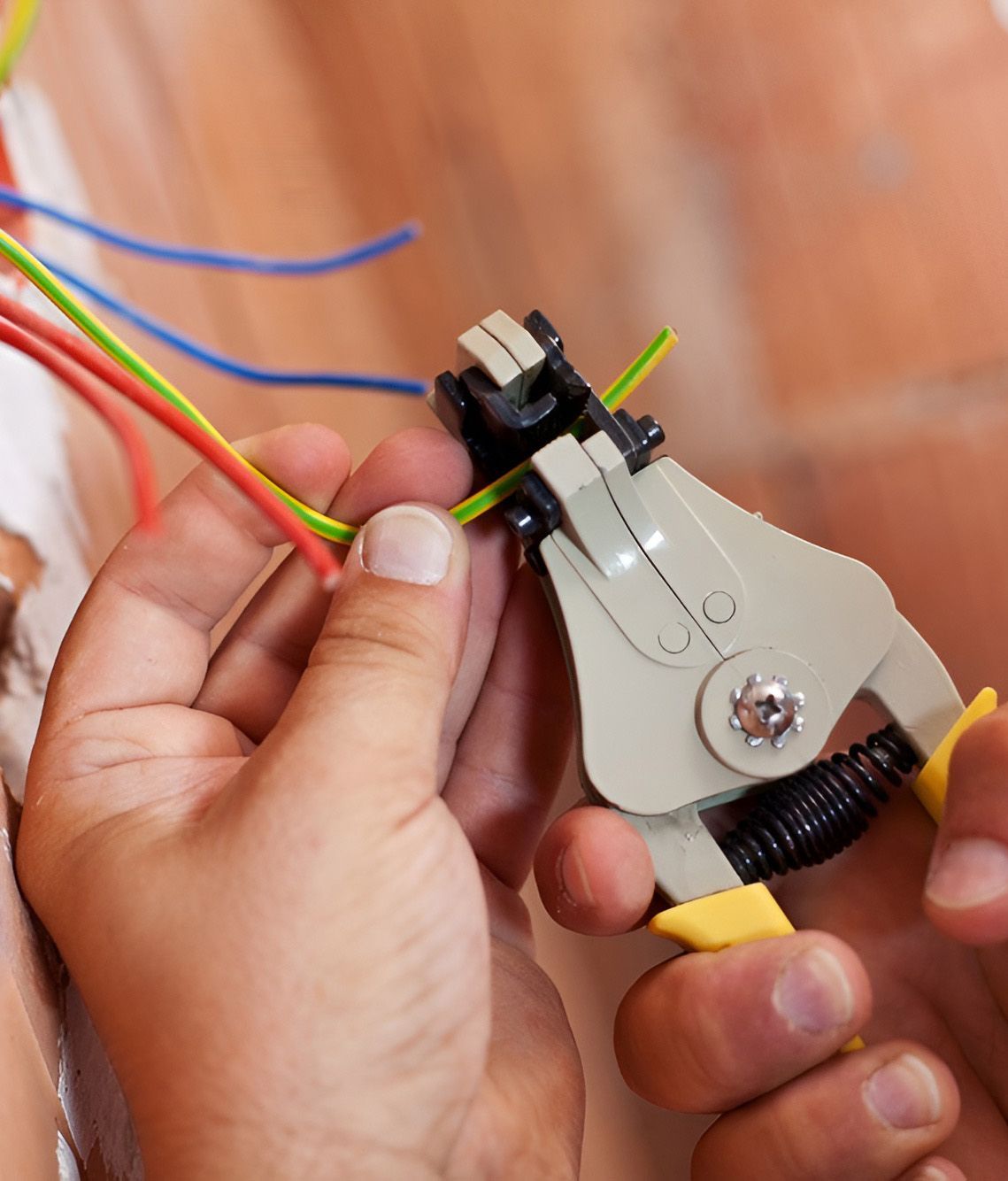 Person Using Wire Stripper on Electrical Wires in a Wall — Electrician in Tamworth, NSW