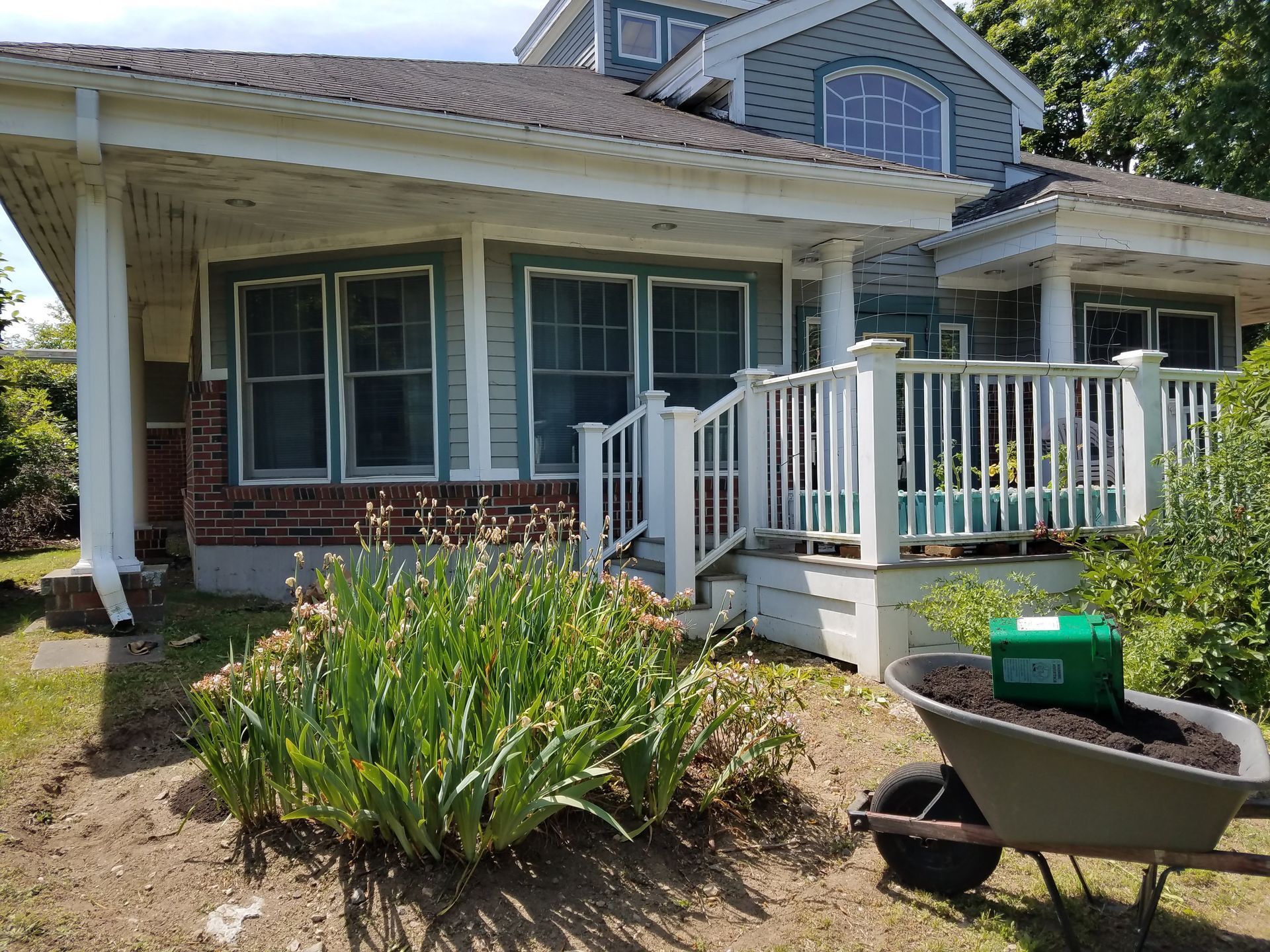 A picture of a flower bed in front of a deck attached to a blue and white building.