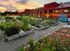 Sunset over Arsenal Park Community Garden with raised beds, flowers, and a lit brick building in the background