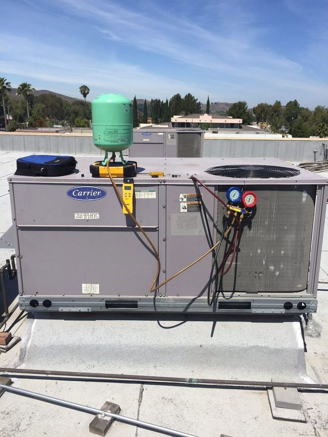 Rooftop HVAC unit with gauges and hoses connected beneath a green pressure tank.