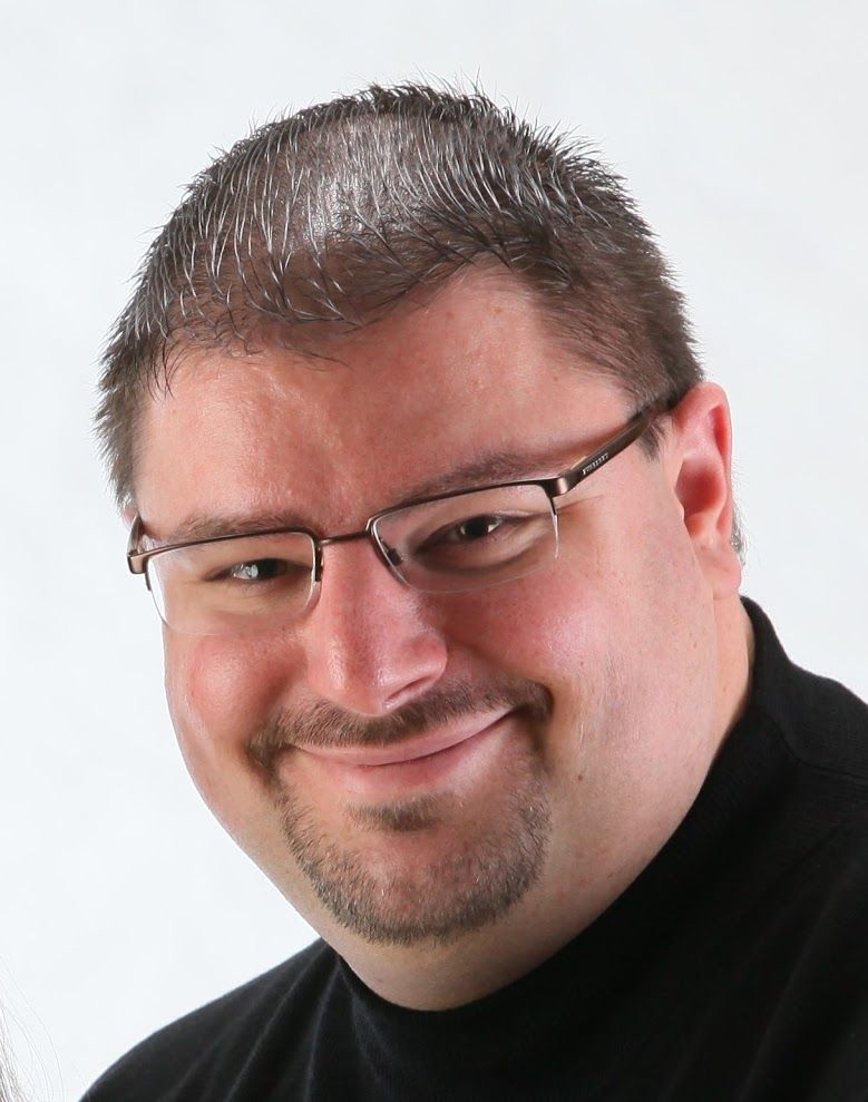 A man wearing glasses and a black shirt smiles for the camera