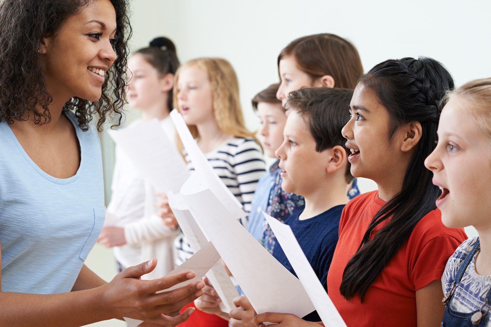A group of children are singing in a choir with a teacher.