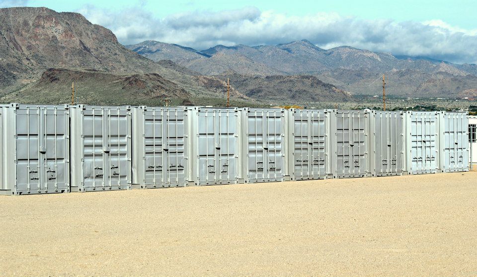 A row of shipping containers in the desert with mountains in the background