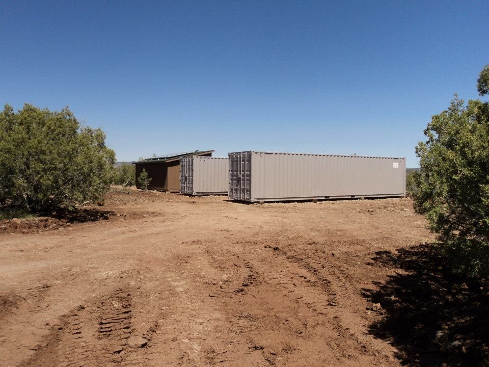 Two shipping containers are parked in a dirt field