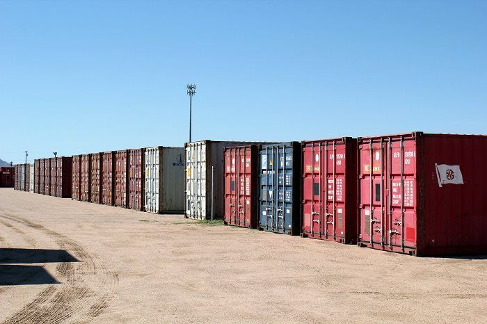 A row of shipping containers are lined up in a dirt lot