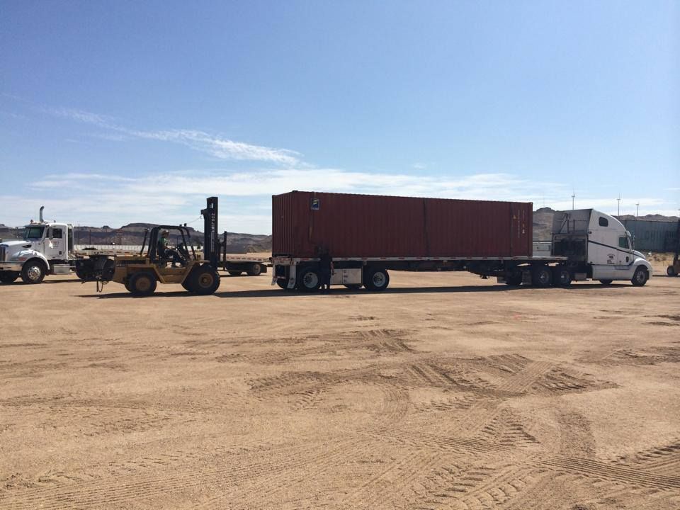 A semi truck is being towed by a forklift in a dirt field.
