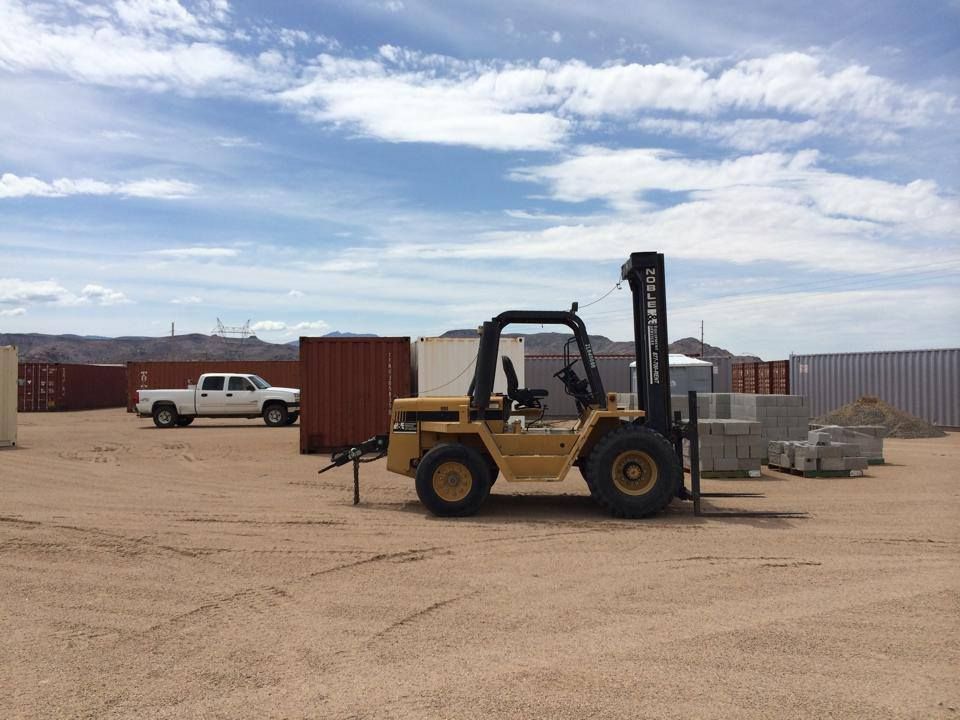 A yellow forklift is parked in a dirt lot.