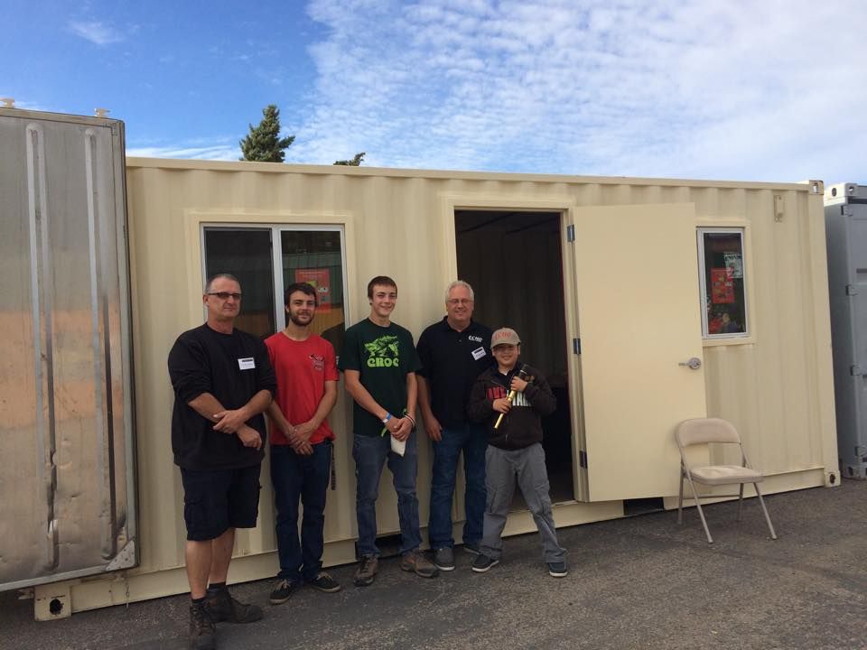 A group of men are standing in front of a shipping container.