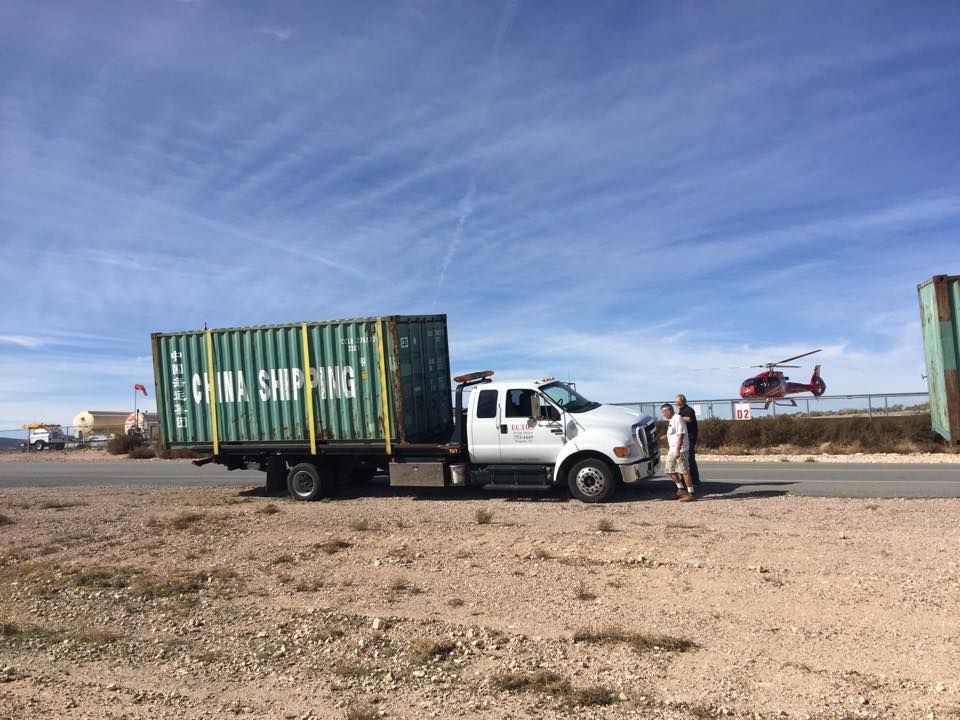 A truck with a green shipping container on the back is parked on the side of the road.