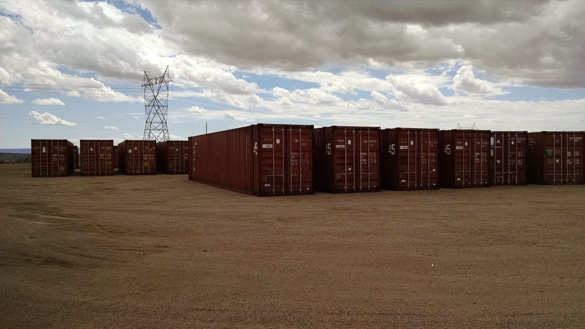 A row of shipping containers sitting on top of a dirt field.