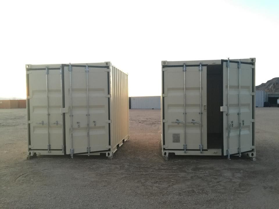 Two shipping containers are sitting next to each other in a dirt field.