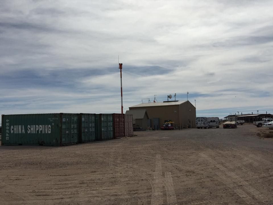 A large green shipping container sits in the middle of a dirt field