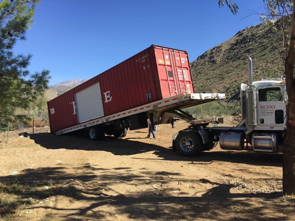 A red shipping container is being towed by a semi truck.