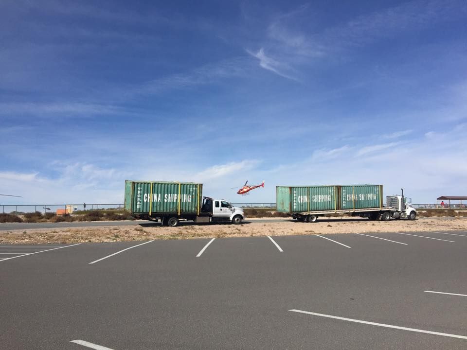 A helicopter is flying over a truck carrying shipping containers